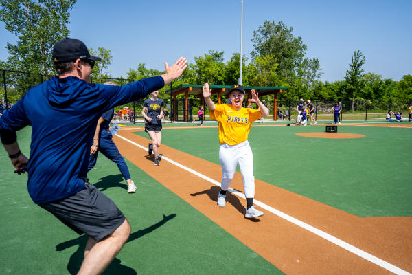 A baseball player coming in to score and getting a high five from a coach.