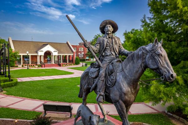 A statue portrays U.S. Marshal Bass Reeves atop a horse holding a gun with his trusty dog running next to him.