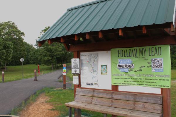 A wooden trailhead with a bench displays a map of the multi-use trails at Ben Geren Park on a cloudy day.
