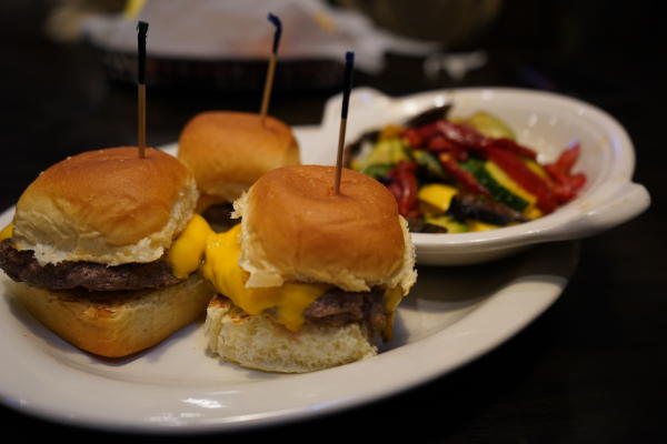 Three burger sliders sit on a plate beside a bowl of grilled vegetables at JJ's Grill in Fort Smith, Arkansas.