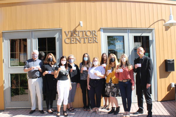 Visit Frederick staff standing in front of the Frederick Visitors Center with masks holding vaccine cards