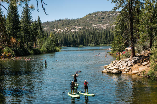 A group of people paddle board along Hume Lake with Sierra Nevada mountains in background