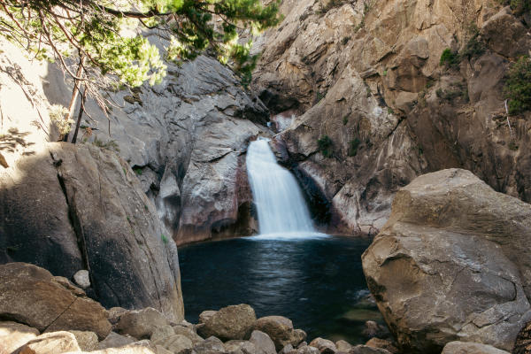 Rushing waterfall splashes into small lagoon with rocks and trees surrounding it