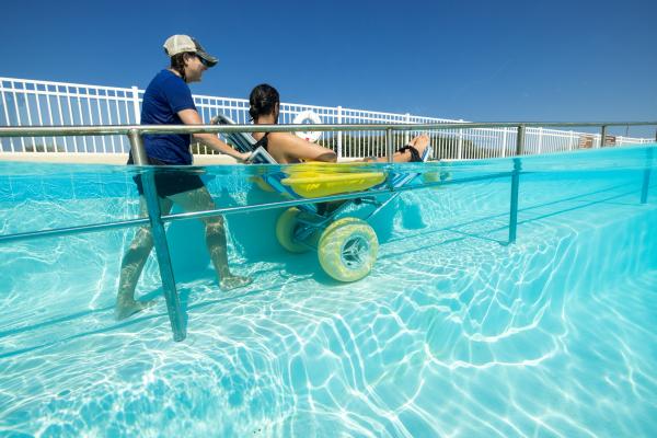 woman pushing man up pool ramp in submersible wheelchair