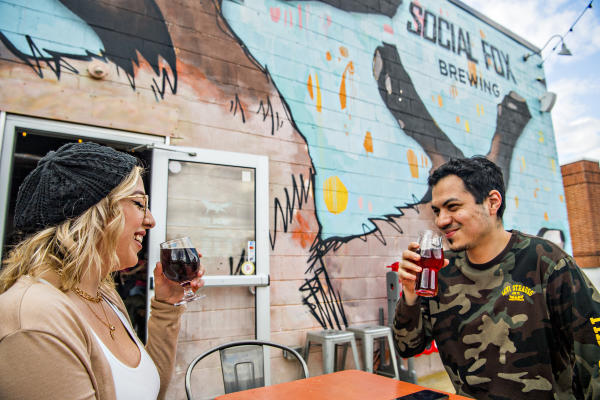 exterior of social fox brewery with large fox mural and man and woman drinking beer