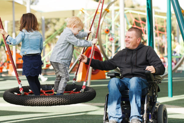 Wheelchair-bound father and kids at the outdoor playground