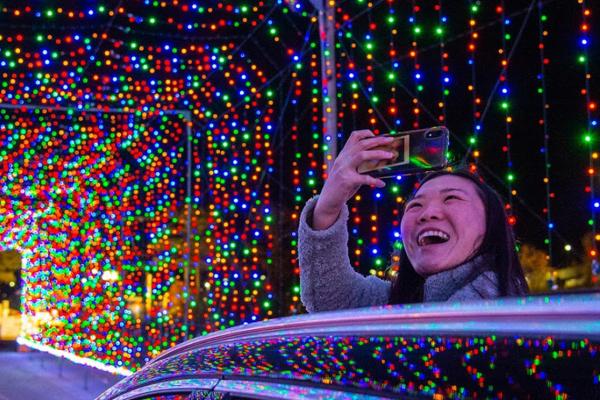 Person taking a cell phone picture in a tunnel covered with holiday lights.