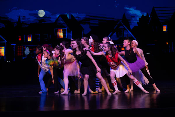 Huntsville Ballet dancers in Halloween costumes perform on stage against a moonlit neighborhood backdrop.