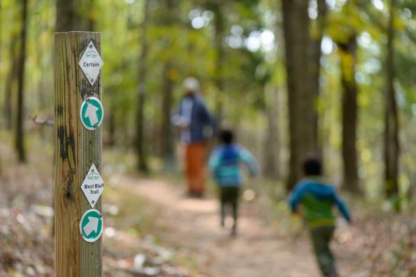Trail marker along a wooded hiking path at Blevins Gap Nature Preserve, with a family walking through the forest in the background.