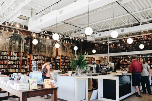 An interior photo of The Dusty Bookshelf store in Manhattan, wooden shelbes on the walls filled with books and customers browsing the selection