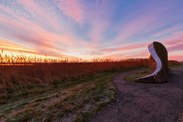 A mirror sculpture surrounded by grassy fields under a dramatic colourful sunset