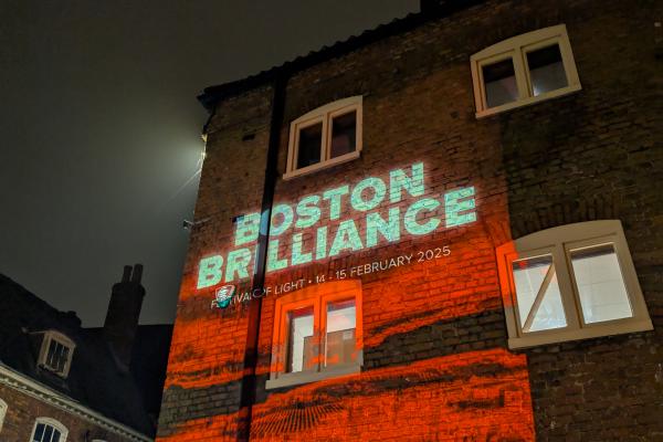 A projection of red light and the outline of buildings on the side of a building at night, promoting Boston Brilliance