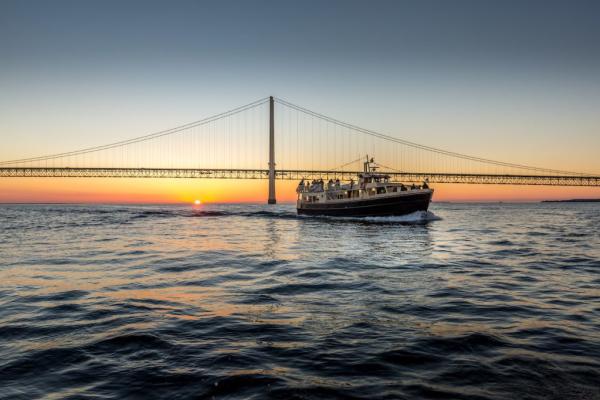 A Mackinac Island Sip ‘n Sail cruise boat passes by the Mackinac Bridge at sunset