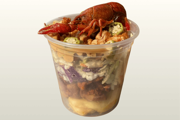 A whole crawfish tops a clear cup layered with macaroni and cheese, meat, coleslaw, okra, beans and sauce.
