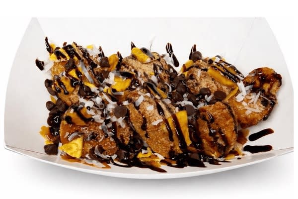 Deep-fried horchata bites topped with chocolate sauce, chocolate chips, shredded coconut and crunchy cereal pieces in a paper tray.