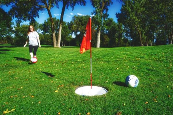 A woman kicking a soccer ball toward a flag on the Footgolf course at Brooklyn Golf Park 