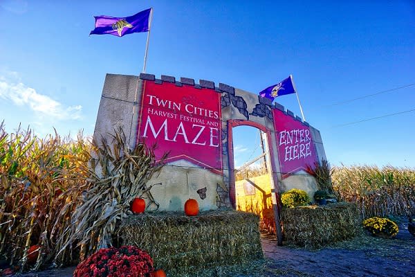 A castle-like façade surrounded by hay bales says "Twin Cities Harvest Festival and Maze. Enter Here"