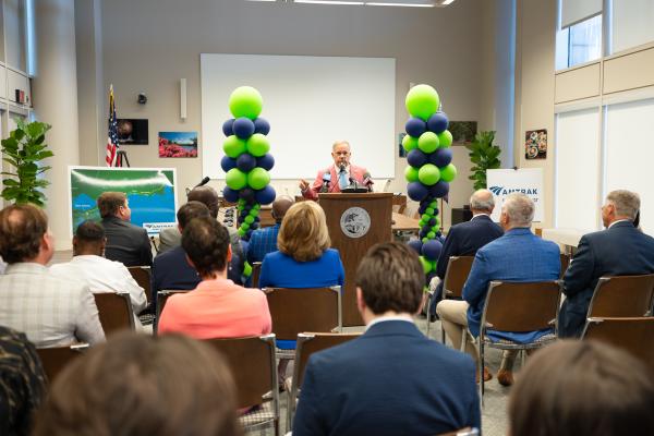 A man wearing a business suit stands behind a podium with green and blue balloons