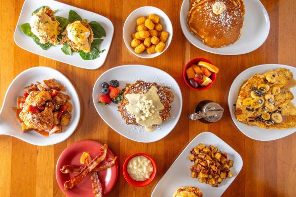 An overhead shot of multiple plates and bowls of breakfast foods, syrups and fruit