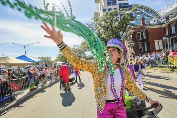 A Mardi Gras reveler in gold sequins and hot pink pants throws green beads to a crowd