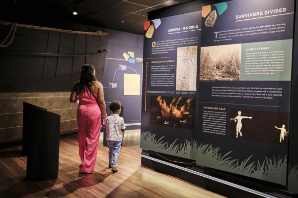 Mother wearing pink jumpsuit walks her child through an exhibit