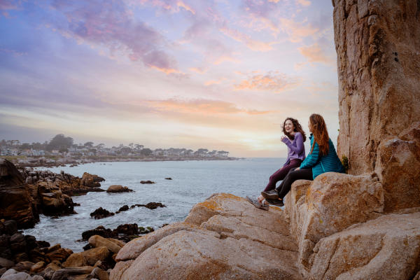 Two girls smiling at sunset on the rocky shores of Pacific Grove in Monterey County