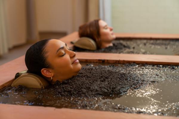 Two women sitting in individual mud baths