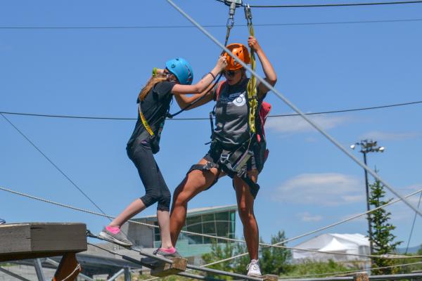 Young Girl gets assistance from adult crossing ropes course