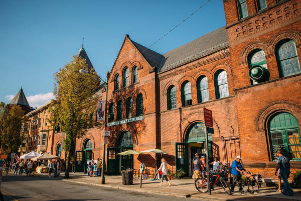 People walk and shop along a street outside a historic red brick building