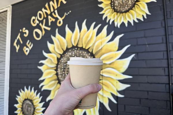 A person holding up a coffee cup in front of a sunflower mural.