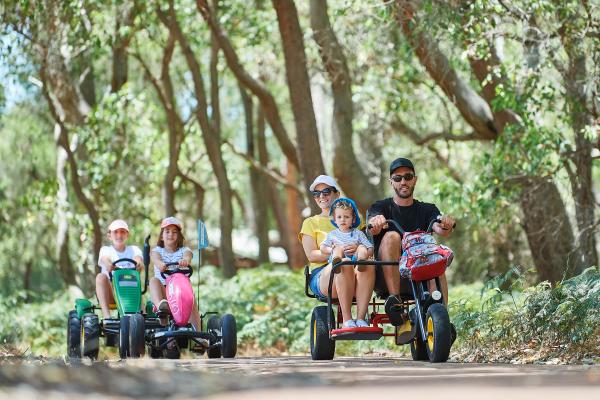 Family and children riding pedal go karts on a path in Whiteman Park.