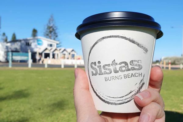 A person holding their coffee cup up in front of the venue, Sistas Burns Beach.
