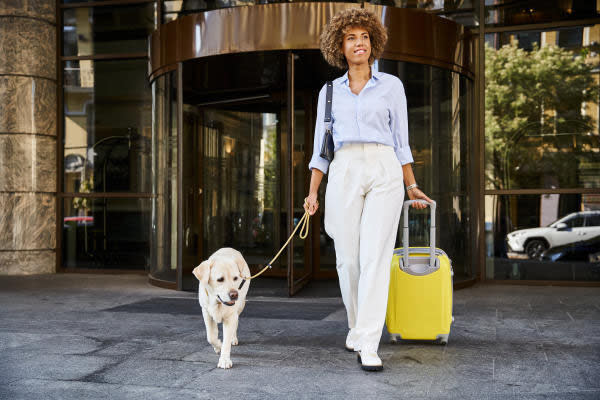 Woman walking with dog at hotel while carrying yellow suitcase