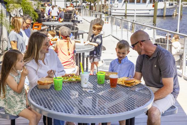 Family dining outdoors at a waterfront restaurant, seated at a table with burgers, fries and drinks along the Tchefuncte River.