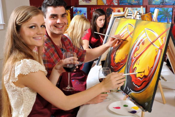 Couple sipping wine and painting a canvas at Painting with a Twist.