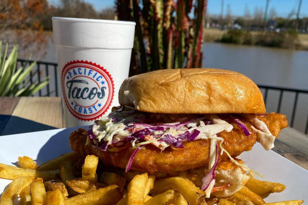 Fries and a fish sandwich with drink on a table outside