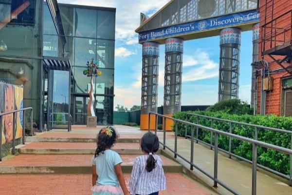 Two girls holding hands in front of the Fort Bend Children's Discovery Center.