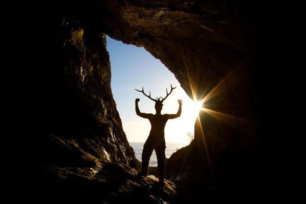A silhouette of a person in a cave wearing antlers.