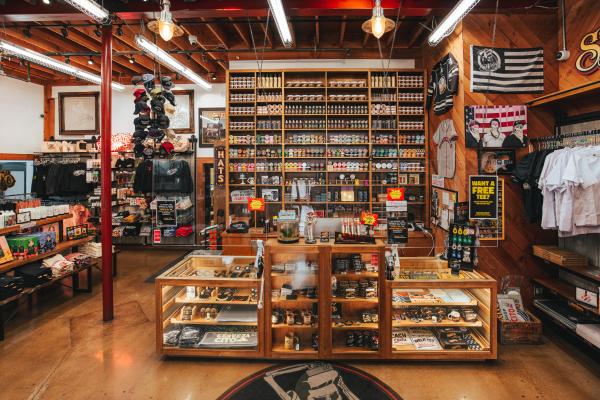 Interior of the Suavecito Store in Santa Ana, showcasing shelves filled with pomades, grooming products, and branded merchandise, along with hats, apparel, and vintage-inspired decor.