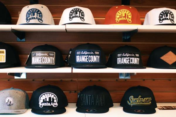 A display of stylish snapback hats at Charlie's Tattoo Supplies in Santa Ana, featuring designs with "Santa Ana" and "Orange County" branding in various colors and styles.