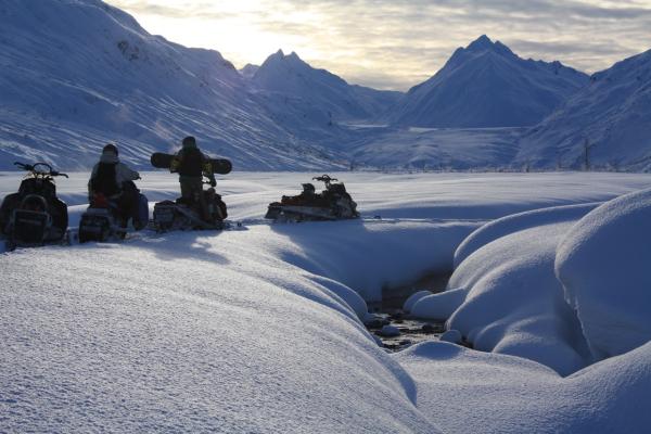 people with snowboards riding on snowmachines in a snowy mountain landscape