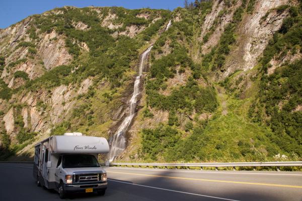 an rv parked alongside a highway by a waterfall in a canyon