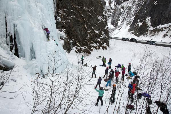 a group of people watching an ice climber ascend a frozen waterfall