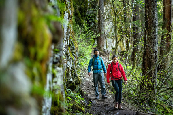 A couple of people hiking along a luscious, green trail through Panther Creek Falls near Vancouver, WA.