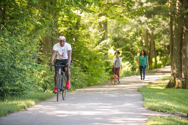 Man riding bike and women walking along wooded rail trail