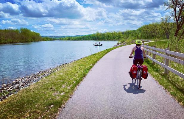 A person wearing a neon green helmet pedals along on a bike along the Erie Canalway Bike Trail