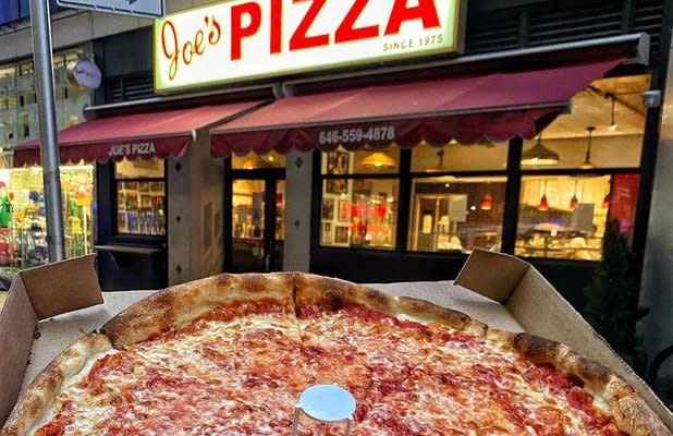 a plain pie held in front of the Joe's Pizza shop sign in NYC