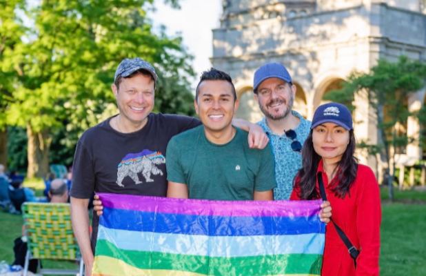 Four people stand in front of the building at Planting Fields holding a Pride Flag