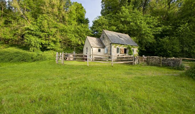 A Cotswold stone cottage surrounded by a wooden fence and backed by trees at Westley Farm
