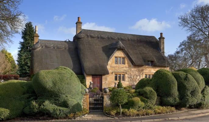 A beautiful thatched cottage surrounded by topiary trees from Manor Cottages in the Cotswolds